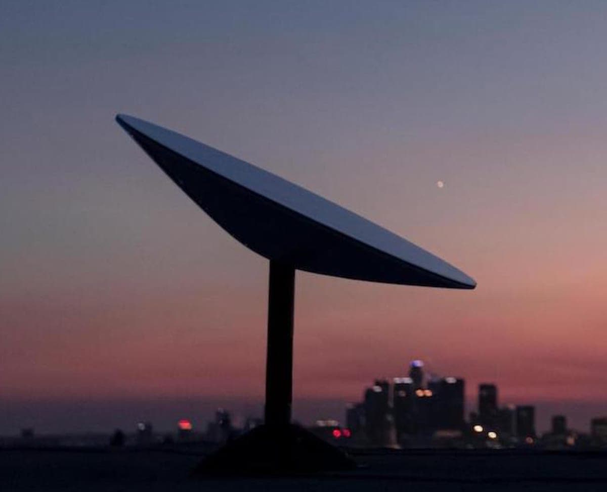 A Starlink satellite dish at sunset, city skyline in the background — remote-location connectivity that rivals metropolitan fiber.